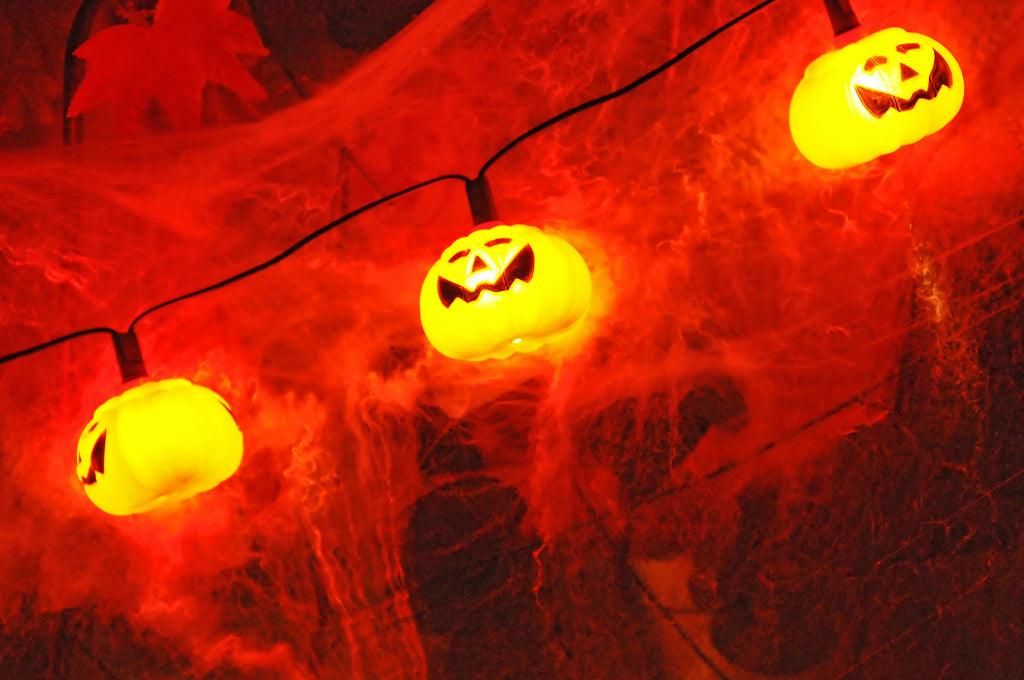 Eine Lichterkette aus kleinen Kürbissen taucht eine gruselige Halloween-Deko in orangefarbenes Licht.