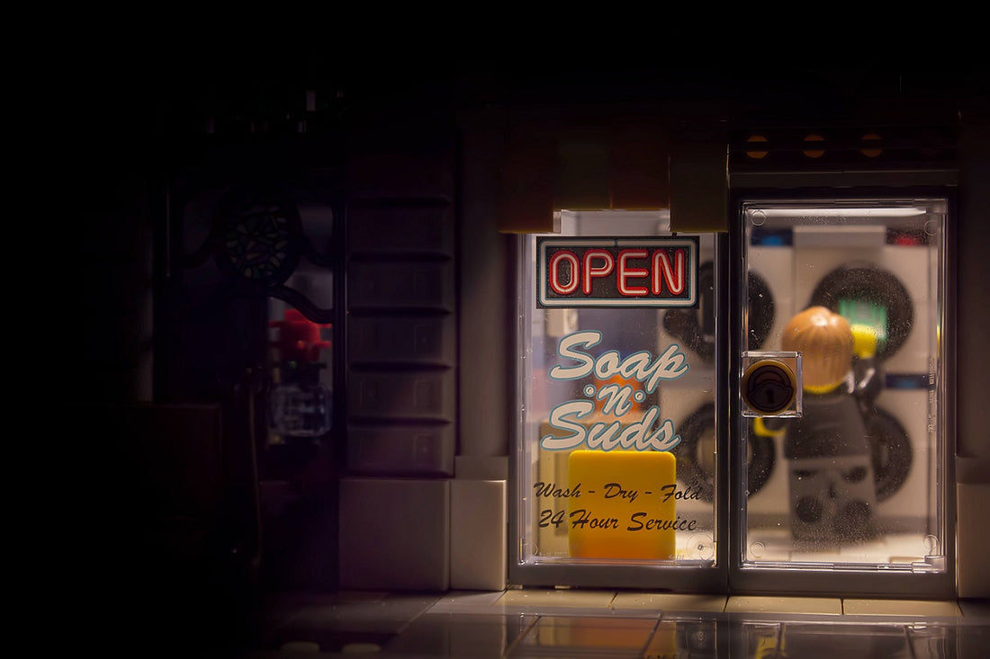 Ein LEGO-Waschsalon, in dem eine Figur drinnen steht und seine Wäsche macht. Der Salon ist von innen und außen beleuchtet.
