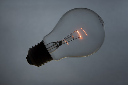 Eine Glühlampe vor grauem Hintergrund, deren Glühfaden leicht glüht