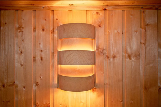 Eine Saunalampe aus gebogenem Holz an der Wand, welche ein angenehmes, indirektes Licht verströmt.