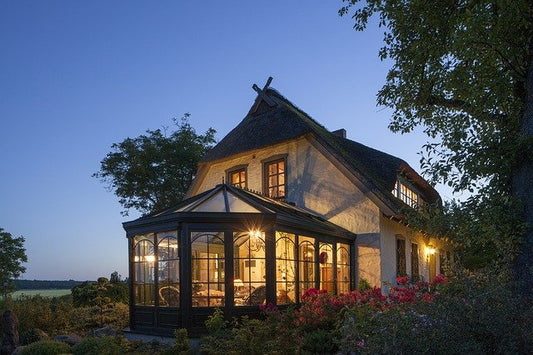 In der Dämmerung sieht man ein Haus mit eingeschalteter Wintrgarten-Beleuchtung.