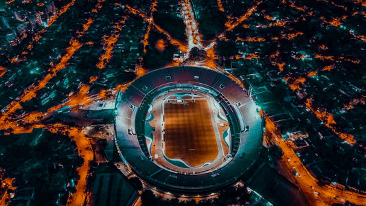 Aus der Vogelperspektive wird der Blick auf ein bei Nacht in Flutlicht erleuchtetes Stadion gerichtet.